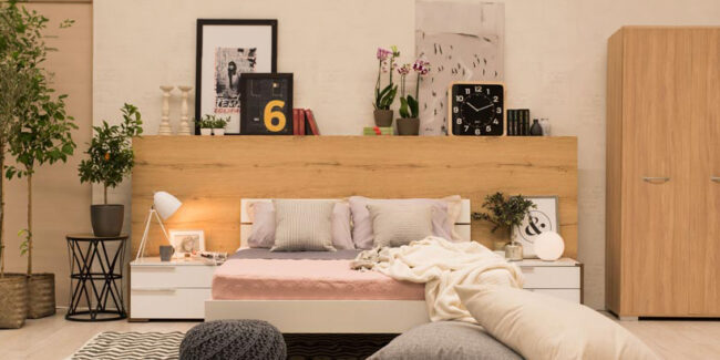 Μια κρεβατοκάμαρα με ένα διπλό κρεβάτι, με μαξιλάρια και ριχτάρια. Δεξιά και αριστερά βρίσκονται δύο κομοδίνα και από πίσω βρίσκεται μια ραφιέρα με πολλά διακοσμητικά δωματίου.