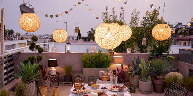 Μια ταράτσα στολισμένη με ένα τραπέζι στην μέση, με φυτά εξωτεικού χώρου αλλά και φωτισμό, όπως φαναράκια αλλά και γιρλάντες ο οποίος δημιουργεί μια ήρεμη και χαλαρή ατμόσφαιρα.