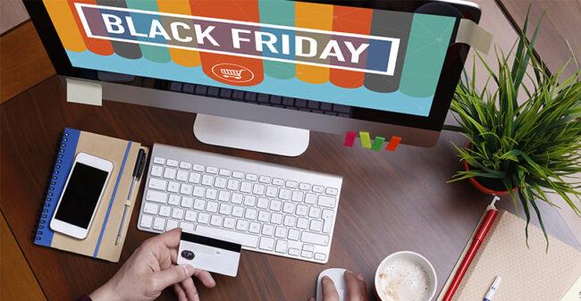 Άτομο που κάνει online αγορές κατά τη διάρκεια προσφορών Black Friday χρησιμοποιώντας έναν επιτραπέζιο υπολογιστή. Στην οθόνη εμφανίζεται το μήνυμα 'Black Friday' με έντονα χρώματα και ένα εικονίδιο καλαθιού αγορών. Το άτομο κρατάει μια πιστωτική κάρτα στο ένα χέρι, ενώ χρησιμοποιεί το ποντίκι για την πλοήγηση, έτοιμο να ολοκληρώσει μια αγορά. Ο χώρος εργασίας περιλαμβάνει πληκτρολόγιο, σημειωματάριο με στυλό, smartphone, μια κούπα καφέ και ένα γλαστράκι, δημιουργώντας ένα μοντέρνο και οργανωμένο περιβάλλον γραφείου
