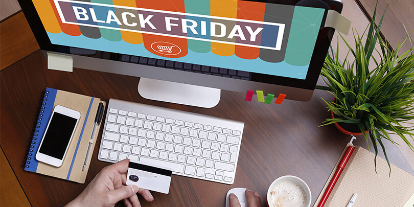 Άτομο που κάνει online αγορές κατά τη διάρκεια προσφορών Black Friday χρησιμοποιώντας έναν επιτραπέζιο υπολογιστή. Στην οθόνη εμφανίζεται το μήνυμα 'Black Friday' με έντονα χρώματα και ένα εικονίδιο καλαθιού αγορών. Το άτομο κρατάει μια πιστωτική κάρτα στο ένα χέρι, ενώ χρησιμοποιεί το ποντίκι για την πλοήγηση, έτοιμο να ολοκληρώσει μια αγορά. Ο χώρος εργασίας περιλαμβάνει πληκτρολόγιο, σημειωματάριο με στυλό, smartphone, μια κούπα καφέ και ένα γλαστράκι, δημιουργώντας ένα μοντέρνο και οργανωμένο περιβάλλον γραφείου